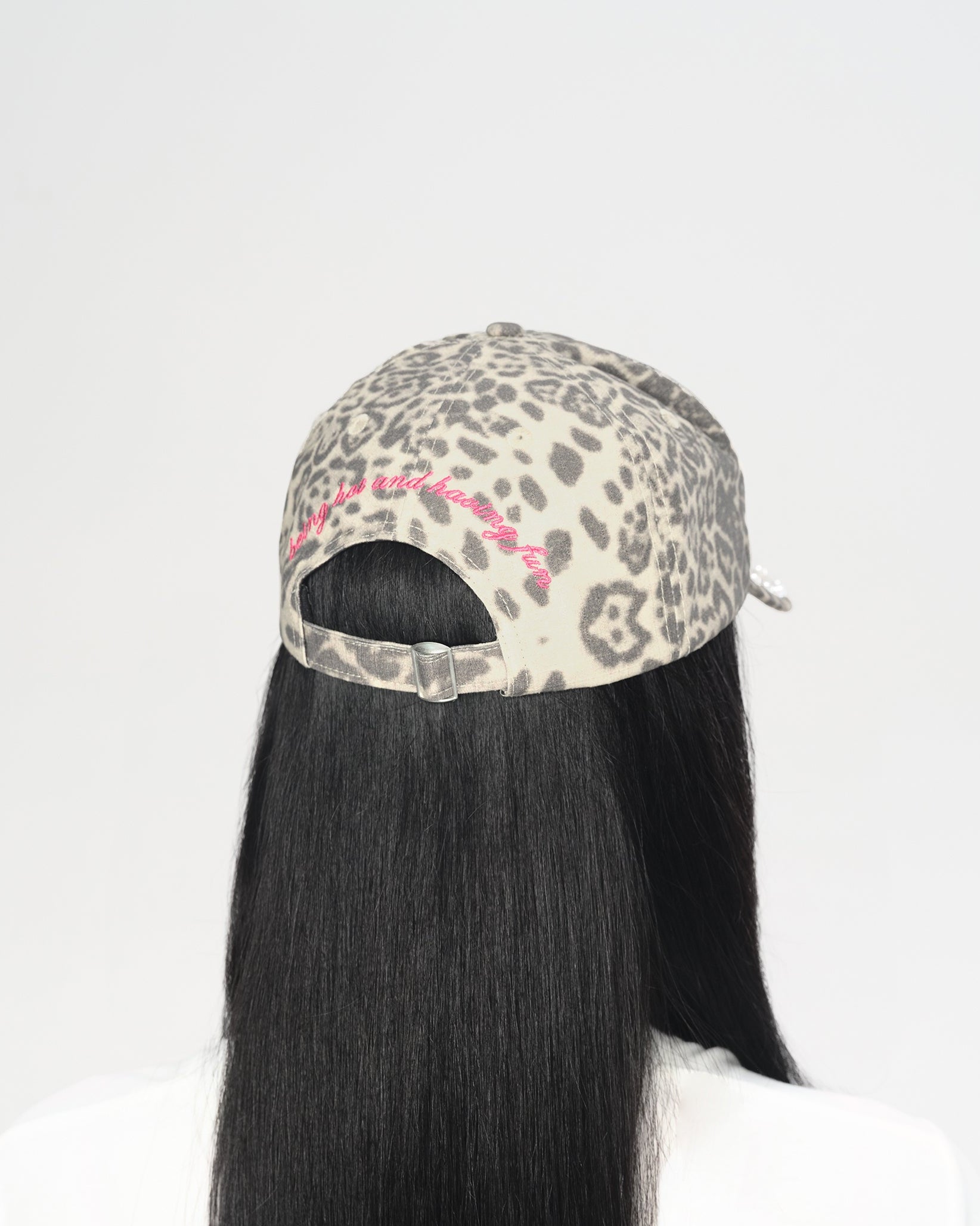 A person shown from the back wearing a leopard-print baseball cap with a pink embroidered detail and long straight black hair, against a plain white background.
