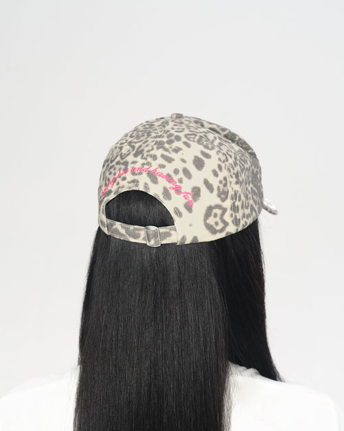 A person shown from the back wearing a leopard-print baseball cap with a pink embroidered detail and long straight black hair, against a plain white background.