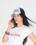 A woman posing in a white graphic t-shirt with red text reading 'FLOP ERA SURVIVOR', paired with leopard print shorts, red lace-up socks, and a black and gray baseball cap with blue text reading 'CULT LEADER'.