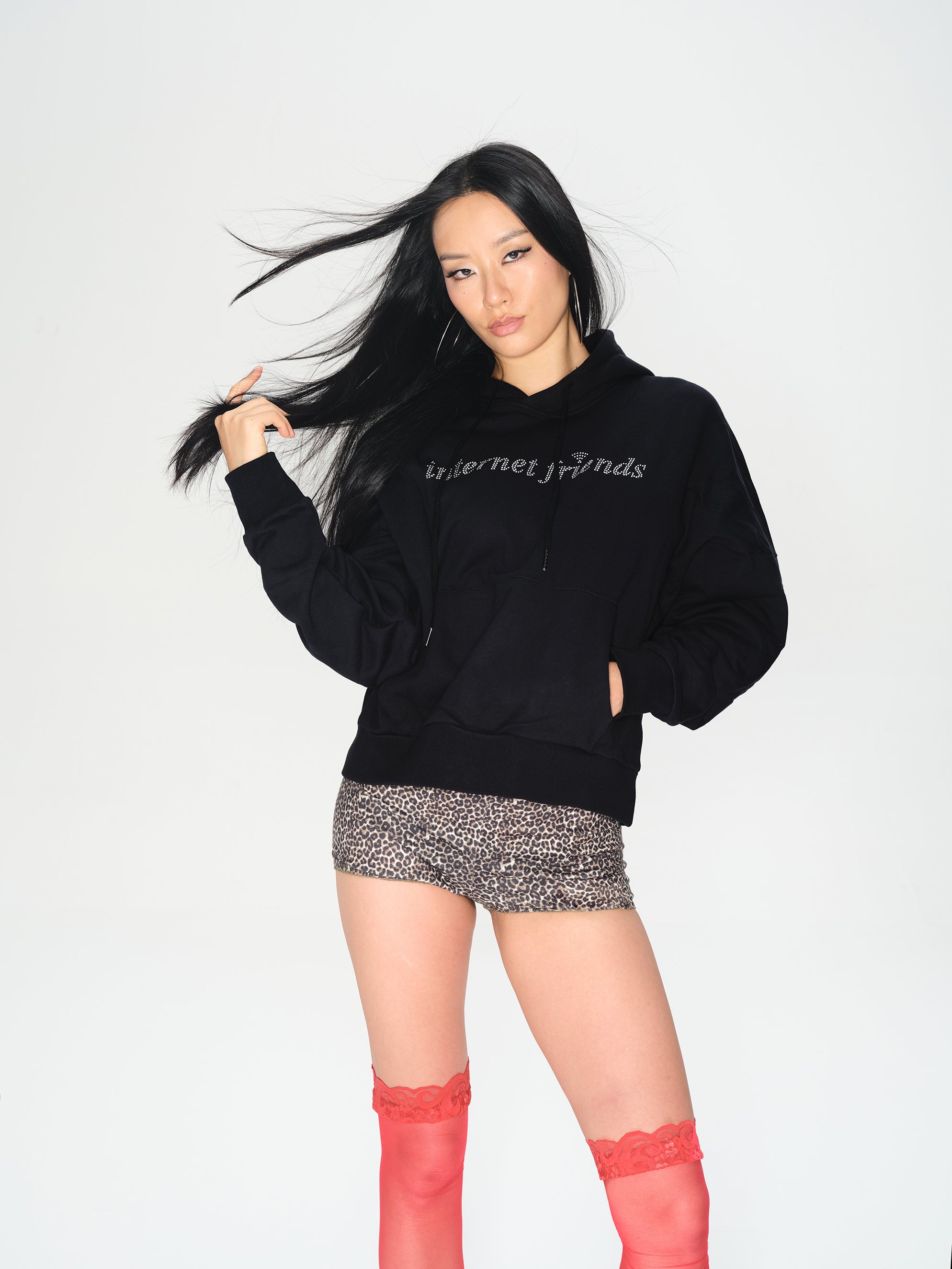 A woman modeling a black hoodie with 'internet finds' printed in white across the chest, paired with a leopard-print mini skirt and red thigh-high socks, against a plain white studio background.