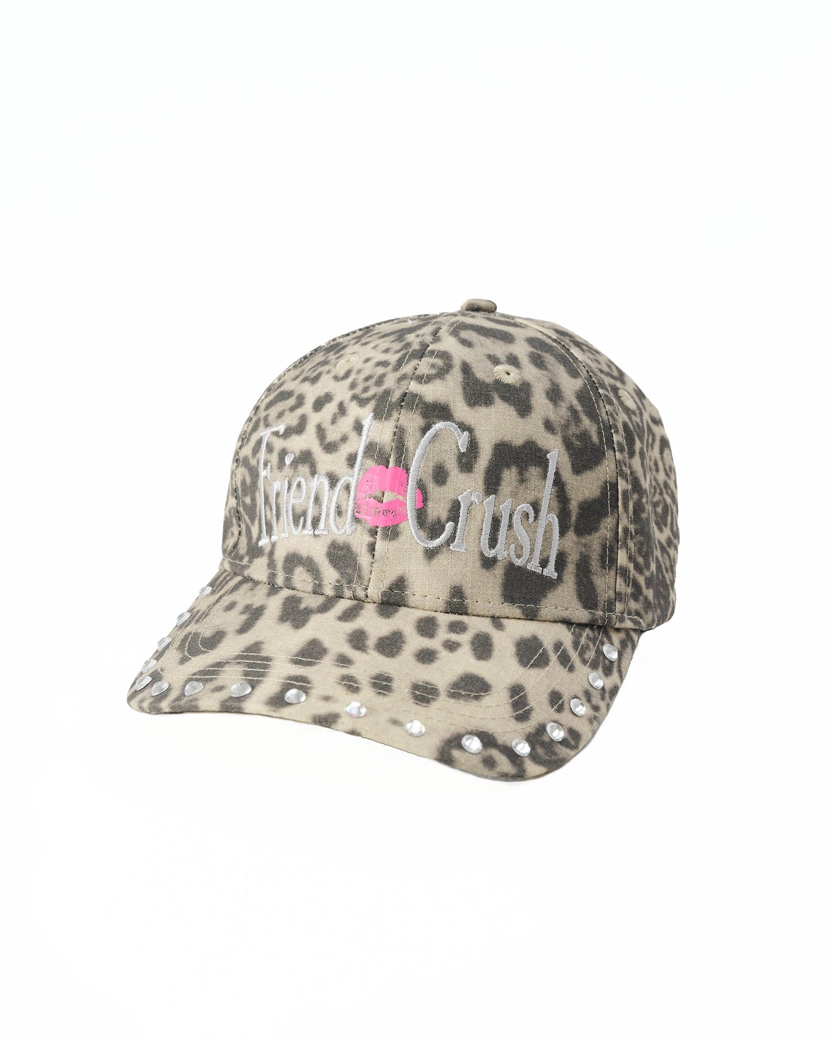 A baseball cap featuring a beige and gray leopard print pattern, with 'friend crush' embroidered in white script across the front and a pink kiss logo in the center.
