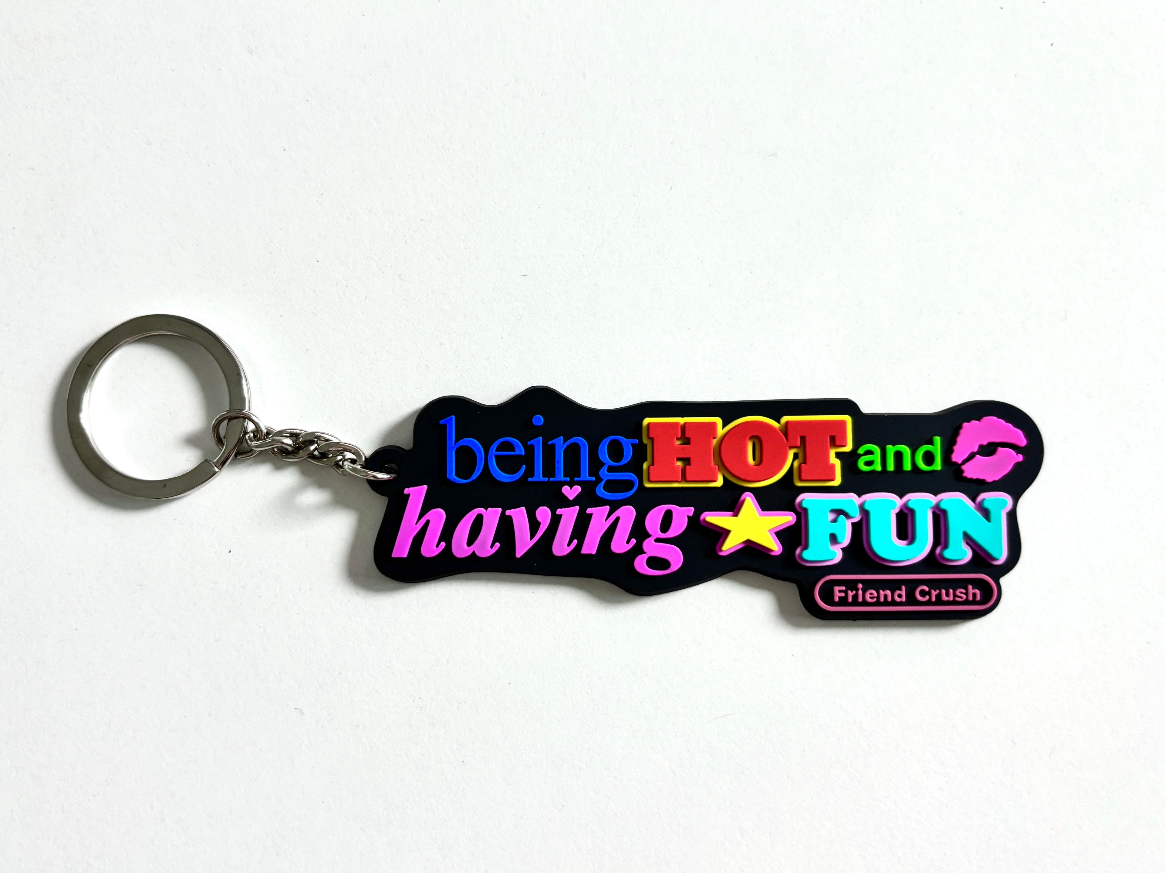 A novelty rubber keychain with a silver split ring, featuring the text 'being HOT and having FUN' in vibrant neon colors on a black background, with 'Friend Crush' written in a small pink badge.
