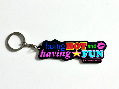A novelty rubber keychain with a silver split ring, featuring the text 'being HOT and having FUN' in vibrant neon colors on a black background, with 'Friend Crush' written in a small pink badge.